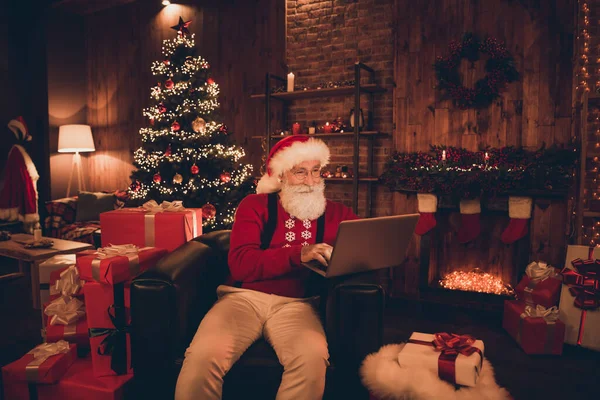 Foto van vrij charmante volwassen man gekleed santa kostuum glimlachen lezen moderne gadget binnen huiskamer — Stockfoto