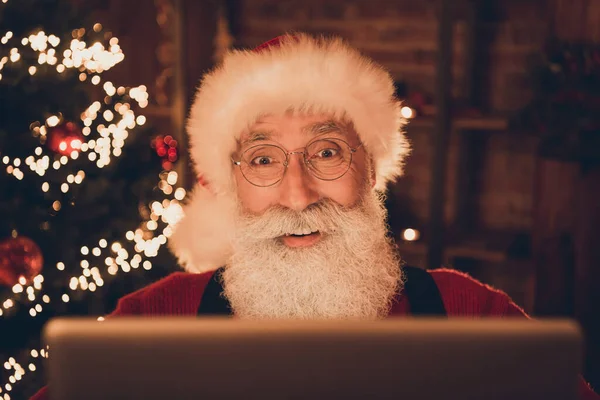 Фото старшего Санта-Клауса счастливая положительная улыбка смотреть читать просматривать монитор компьютера виртуальный декор огни Рождества в помещении — стоковое фото