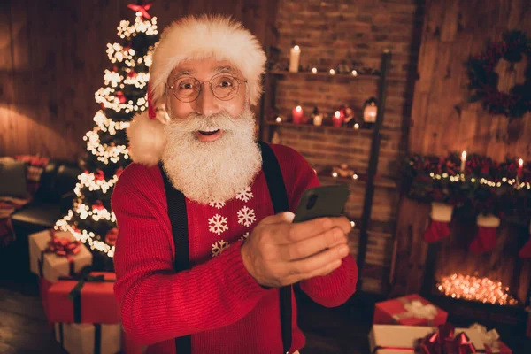 Фото изумленного смешного Санта Клауса держать телефон открытым ртом носить шляпу пуловер в северном полюсе офиса в помещении — стоковое фото
