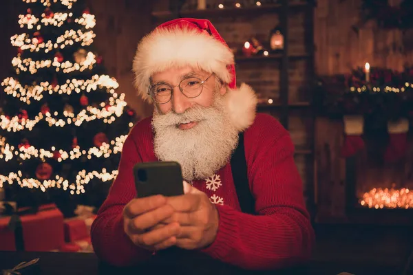 Photo of cheerful santa claus look take remote phone order wear hat pullover in north pole office indoors — Stock Photo, Image