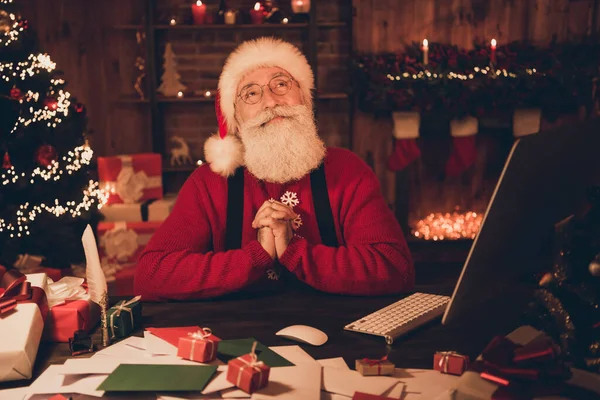 Фото мечтательного Санта-Клауса сидеть рабочее место держаться за руки думать носить шляпу свитер в северном полюсе офиса в помещении — стоковое фото