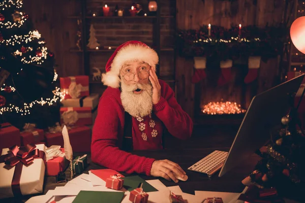 Foto von verblüfft sprachlos Weihnachtsmann nehmen PC-Lieferauftrag tragen Hut Pullover in Nordpol-Büro drinnen — Stockfoto