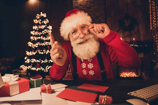 Фотопортрет Санта Клаус сидит за столом в комнате рядом с украшенной рождественской елкой улыбаясь давая совет жестом руки — стоковое фото