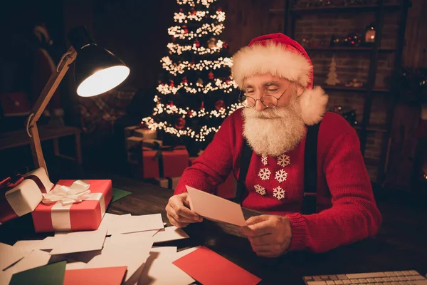 Φωτογραφία του χαρούμενου ωραίο santa claus sit table σκούρο βράδυ διαβασμένο γράμμα φορούν καπέλο πουλόβερ στο βόρειο πόλο γραφείο σε εσωτερικούς χώρους — Φωτογραφία Αρχείου