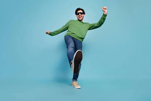 Foto in voller Größe von jungen gut aussehenden Mann in Sonnenbrille tanzen Diskothek heben Bein isoliert auf blauem Hintergrund — Stockfoto
