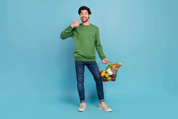 年轻笑容满面的男子去购物的全幅照片，购买带有蓝色背景的大拇指标志的食品杂货 — 图库照片