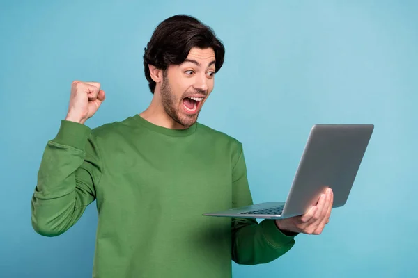 젊고 흥분 한 쾌활 한 청년 이 푸른 색 배경에 고립된 노트북을 사용하여 승리의 주먹을 드는 모습 — 스톡 사진