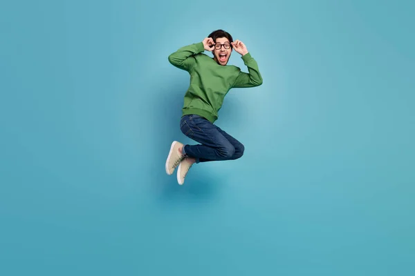 Foto in voller Größe von glücklich Gute-Laune-Kerl in Brille springen erregte Emotionen tragen grünen Pullover isoliert auf blauem Hintergrund — Stockfoto