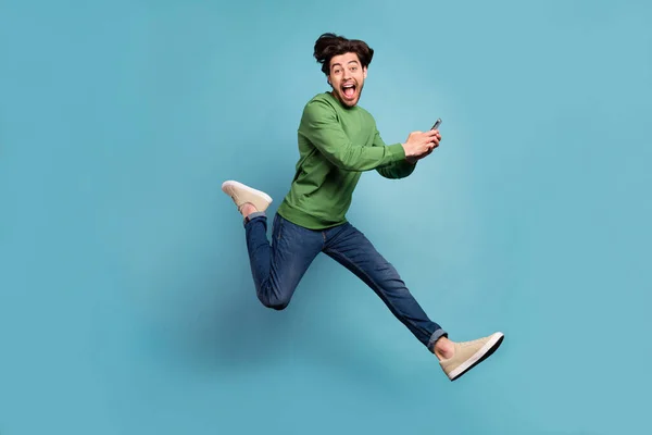 Full size profiel zijkant foto van funky opgewonden man springen verslaafd aan sociale media hold telefoon geïsoleerd op blauwe kleur achtergrond — Stockfoto