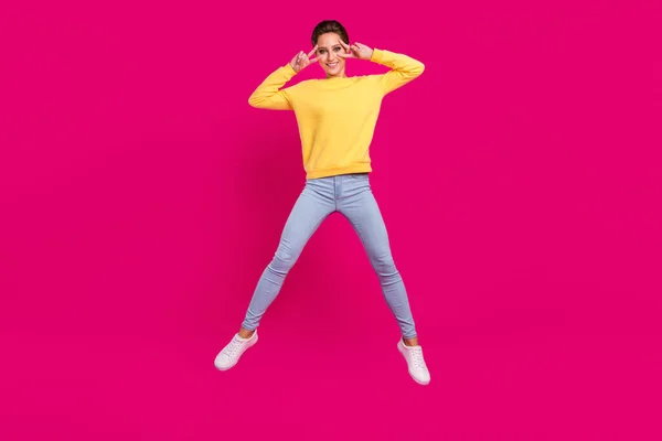 Foto av rolig charmig ung dam bära gul jumper leende hoppa högt visar v-tecken täcka ögon isolerad rosa färg bakgrund — Stockfoto