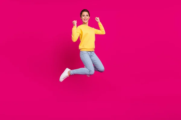 Foto de la encantadora joven excitada usar jersey amarillo sonriente saltando puños altos aislados de color rosa de fondo —  Fotos de Stock