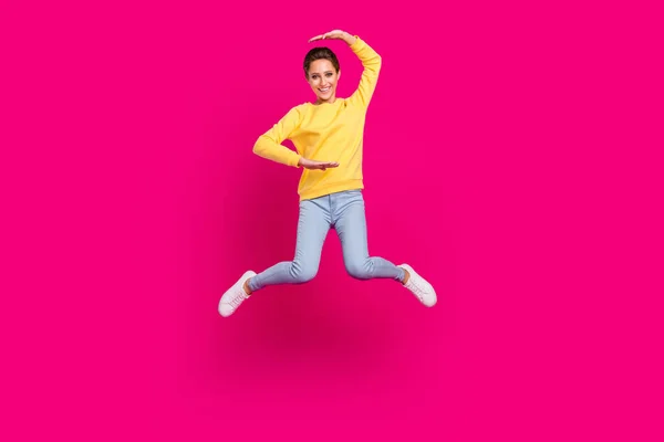 Вид в полный рост на привлекательную жизнерадостную девушку, прыгающую, показывая размер, изолированный на ярко-розовом фоне — стоковое фото