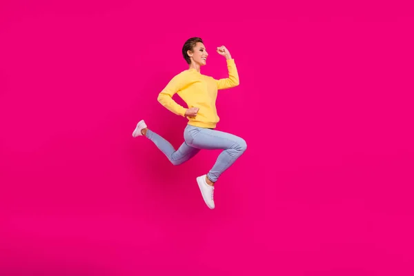 Foto de divertida encantadora joven vestida de amarillo jersey saltando corriendo rápido sonriendo aislado color rosa fondo —  Fotos de Stock