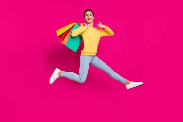 Photo de funky douce jeune femme porter pull jaune sautant bonnes affaires attente montrant pouce vers le haut isolé fond de couleur rose — Photo