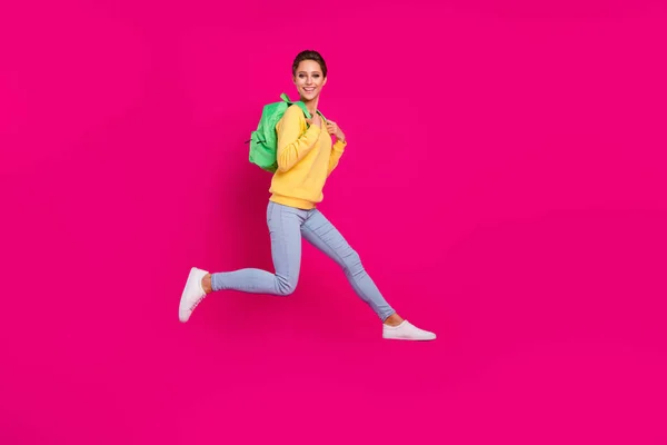 Фото очаровательной милой молодой женщины одета желтый рюкзак пуловер прыжки улыбаясь изолированный розовый цвет фона — стоковое фото