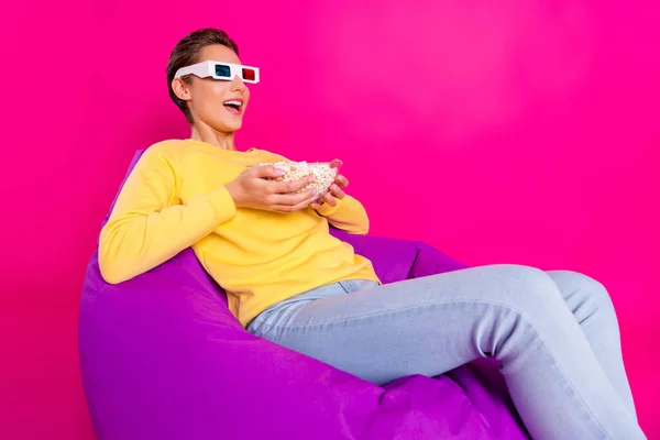 Bild av imponerad rolig ung dam bära gul tröja 3d glasögon sittande böna väska äta popcorn isolerad rosa färg bakgrund — Stockfoto