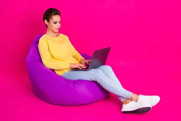 Potret menarik fokus gadis duduk di kursi tas menggunakan laptop mengetik terisolasi di atas warna merah muda cerah latar belakang — Stok Foto