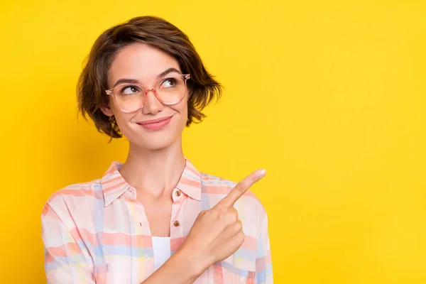 Foto van dromerige mooie jonge vrouw wijzen vinger verkoop lege ruimte slijtage bril geïsoleerd op gele kleur achtergrond — Stockfoto