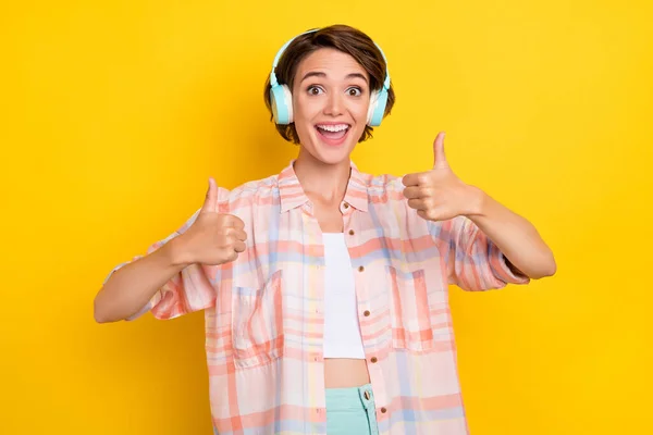 Porträtt av attraktiva bedövade lycklig glad flicka lyssna hit visar tummen överens isolerad över ljusgul färg bakgrund — Stockfoto