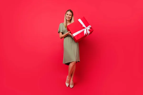 Foto de engraçado encantador jovem vestido roupas verdes segurando grande caixa de presente sorrindo isolado fundo de cor vermelha — Fotografia de Stock