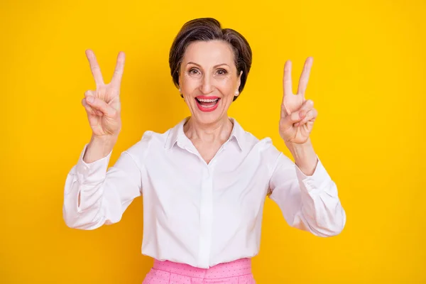 Foto von glänzenden entzückenden reifen Dame tragen weiße Kleidung zeigt zwei V-Zeichen lächeln isoliert gelbe Farbe Hintergrund — Stockfoto