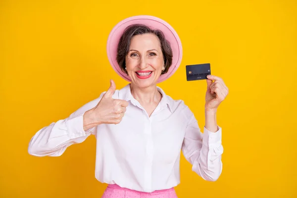 Foto von reifen Geschäftsfrau glücklich positives Lächeln Daumen hoch wie Werbung Wahl Kreditkarte isoliert über gelben Farbhintergrund — Stockfoto