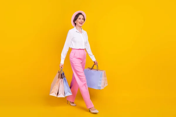 Profil complet du corps photo latérale de la femme âgée heureux sourire positif aller marcher sacs de soute shopping isolé sur fond de couleur jaune — Photo