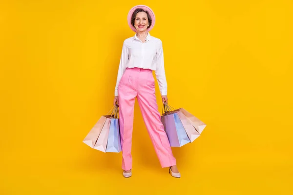 Full längd foto av äldre kvinna glad positiv leende hålla väskor butik kund försäljning isolerad över gul färg bakgrund — Stockfoto