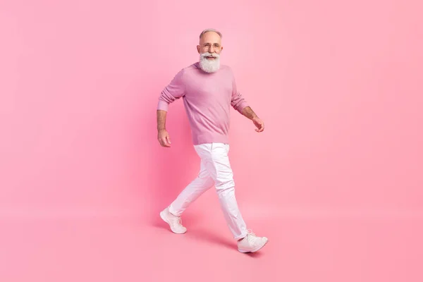 Foto de homem maduro atraente bonito vestido pulôver óculos sorrindo andando isolado cor de rosa fundo — Fotografia de Stock