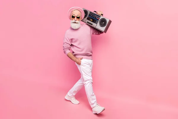 Full size profiel foto van optimistisch grijs haar oude man gaan met boom box slijtage brillen trui geïsoleerd op roze achtergrond — Stockfoto