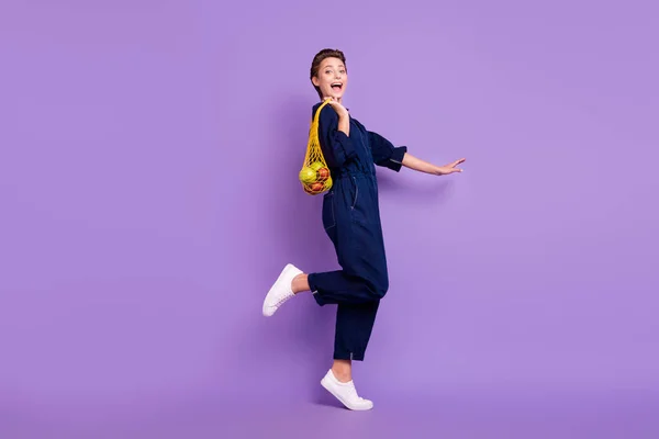 Πλήρες μέγεθος προφίλ πλευρά φωτογραφία του νεαρού ενθουσιασμένοι χαμογελαστό κορίτσι πάει βόλτα ψώνια επαναχρησιμοποιήσιμη τσάντα δίχτυ απομονώνονται σε βιολετί χρώμα φόντο — Φωτογραφία Αρχείου