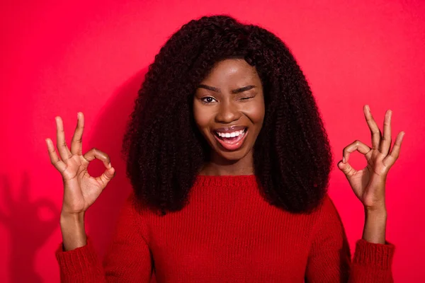 Foto von jungen schwarzen Mädchen glücklich positives Lächeln Augenzwinkern zeigen okay okay Zeichen Anzeige isoliert über rotem Hintergrund — Stockfoto