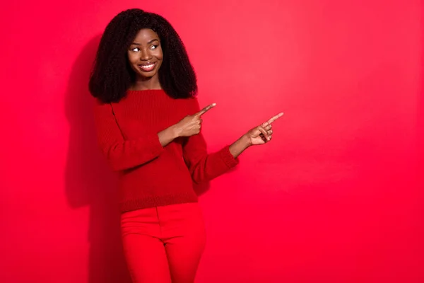 Foto de menina negra feliz sorriso positivo olhar indicar dedos espaço vazio anúncio escolha promo isolado sobre fundo de cor vermelha — Fotografia de Stock