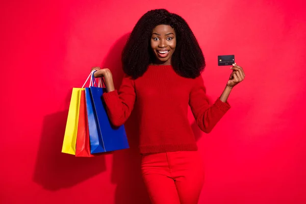 Genç siyah kızın fotoğrafı mutlu bir gülümseme içinde alışveriş torbaları, kredi kartı satışları kırmızı arka planda izole edilmiş. — Stok fotoğraf