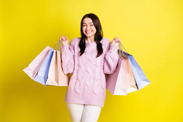 Foto de dulce dama sostiene muchas bolsas hacen compras usan suéter pantalones blancos aislados en fondo de color amarillo vivo —  Fotos de Stock