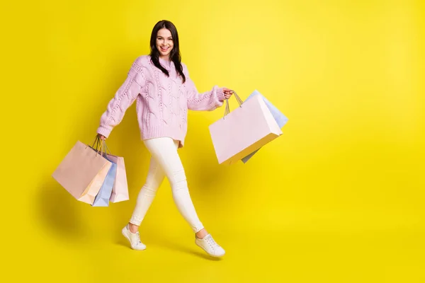 Full body profile photo of excited millennial lady hold bags go wear pink sweater pants isolated on yellow color background