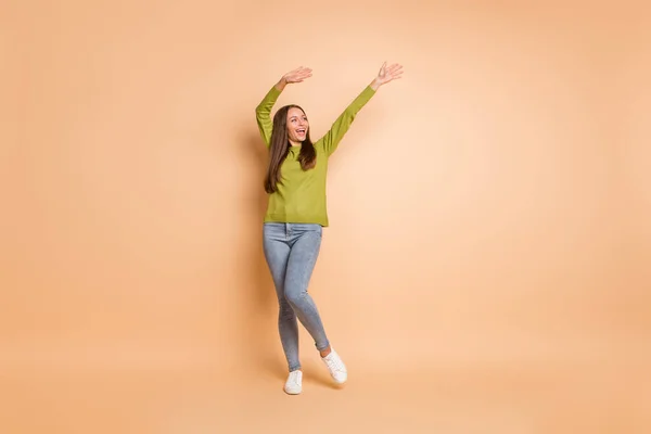 Foto de longitud completa de niña levantar las manos buscar espacio vacío usar suéter verde calzado pantalones aislados de color beige fondo — Foto de Stock