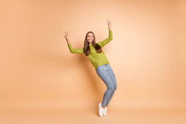 Volledige foto van lady tiptoes tonen twee v-tekens dragen groene trui schoeisel jeans geïsoleerde beige kleur achtergrond — Stockfoto
