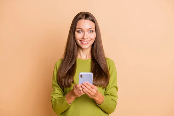 Fénykép vidám vicces lány tart telefon néz kamera fényes mosoly viselni zöld pulóver elszigetelt bézs színű háttér — Stock Fotó