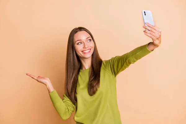 Zdjęcie pani trzymać telefon zrobić selfie ramię trzymać puste miejsce nosić zielony pullover odizolowany beżowy kolor tło — Zdjęcie stockowe
