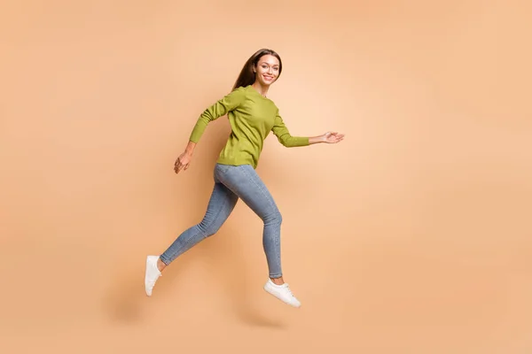 プロフィール写真のエネルギッシュな女の子ジャンプ行く服緑セータージーンズスニーカー隔離ベージュ色背景 — ストック写真
