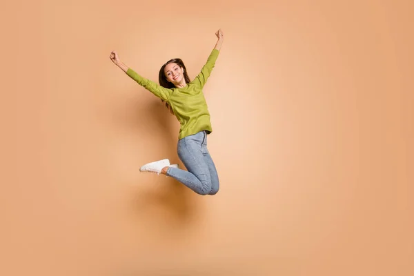 Foto van actieve meisje springen verhogen handen omhoog dragen groene trui jeans sneakers geïsoleerde beige kleur achtergrond — Stockfoto