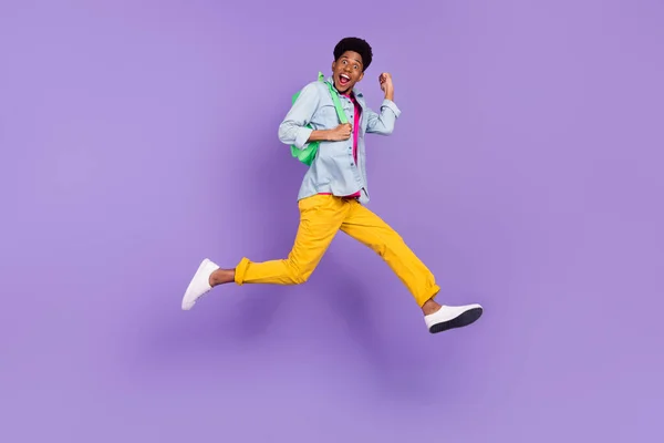 Foto von fröhlichen Kerl springen Eile laufen erhöhen Faust tragen Rucksack blaues Hemd isoliert lila Farbe Hintergrund — Stockfoto
