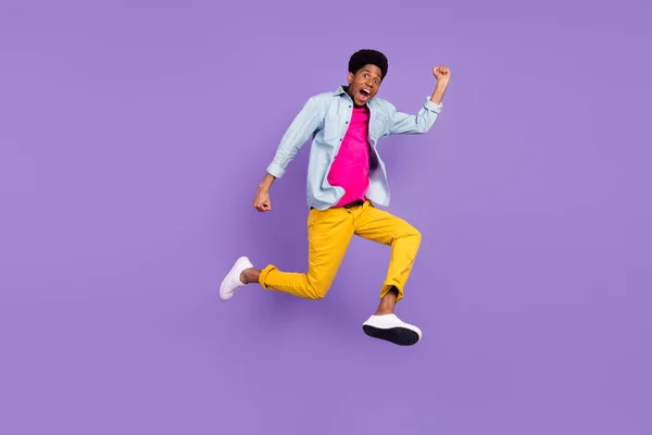Foto de chico ganador saltar levantar los puños regocijarse correr usar azul camisa pantalones zapatos aislados color púrpura fondo —  Fotos de Stock