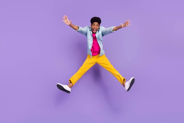 Foto de chico loco inspirado salto levante las manos boca abierta desgaste azul camisa pantalones zapatos aislados color púrpura fondo — Foto de Stock
