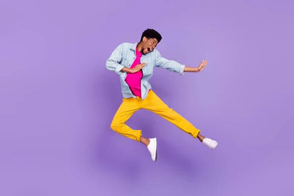 Foto de perfil del chico afro activo asombrado salto pierna golpeada usar pantalones de camisa azul zapatillas aisladas color púrpura fondo — Foto de Stock