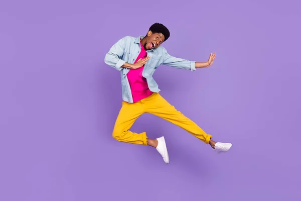 Foto av vårdslös funky energisk kille hoppa spark ben bära blå skjorta byxor sneakers isolerad lila färg bakgrund — Stockfoto