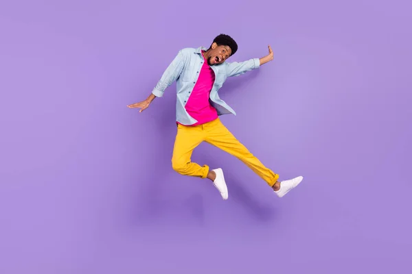 Fotografie sportovního bláznivý bezstarostný chlap skok vzrušený tvář nosit modré košile kalhoty tenisky izolované fialové barvy pozadí — Stock fotografie