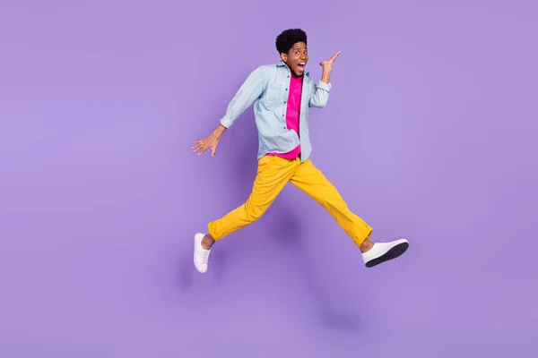 Fotografie sportovního běžec chlap skok pohyb křičet otevřená ústa nosit modré košile kalhoty izolované fialové barvy pozadí — Stock fotografie