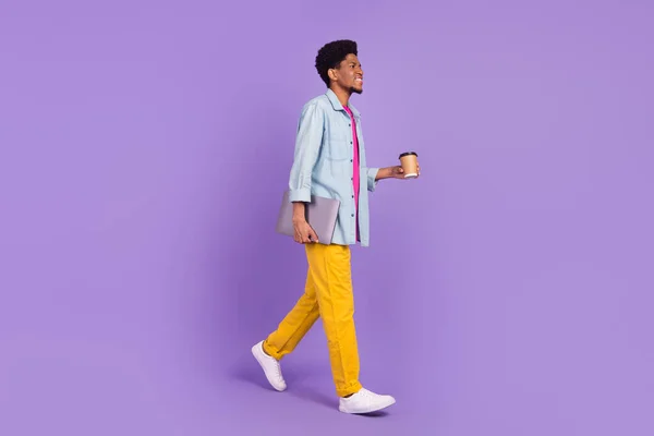 Foto de hombre lindo funky desgaste vaquero caminar bebiendo té buscando espacio vacío sosteniendo gadget aislado color púrpura fondo —  Fotos de Stock